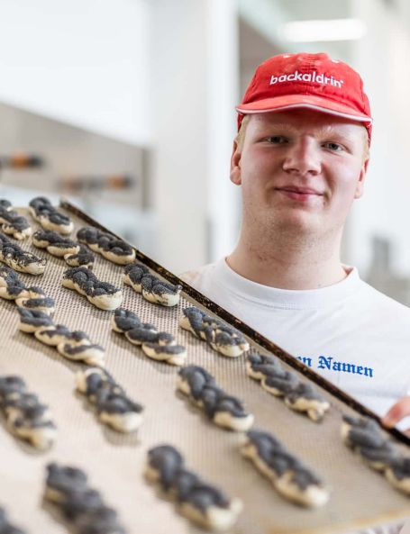 Sailer Lehrling hält Backblech mit Mohnzöpfen